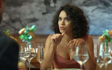 Xaviera (Giovana Cordeiro) com expressão séria em uma mesa de restaurante em Mar do Sertão