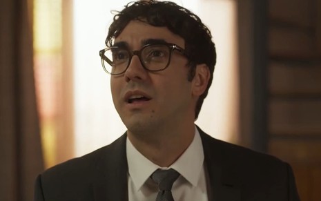 Gabriel Godoy caracterizado como Márcio Castro; ator usa terno preto e óculos em cena de Mar do Sertão