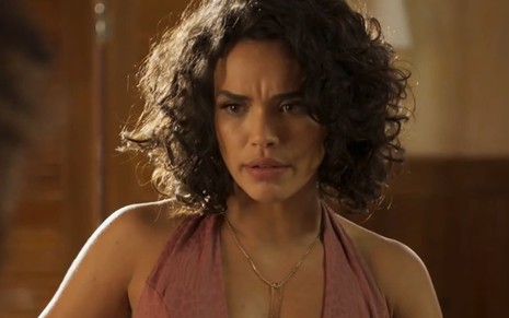 Giovana Cordeiro, caracterizada como Xaviera, dá um sorriso de lado em cena de Mar do Sertão; atriz tem o cabelo na altura dos ombros e veste
