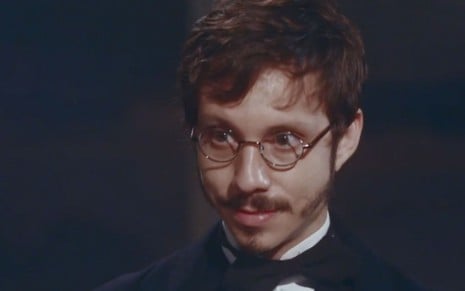João Pedro Zappa em cena de Nos Tempos do Imperador: caracterizado como Nélio, ator está em close e olha com atenção alguém fora do quadro
