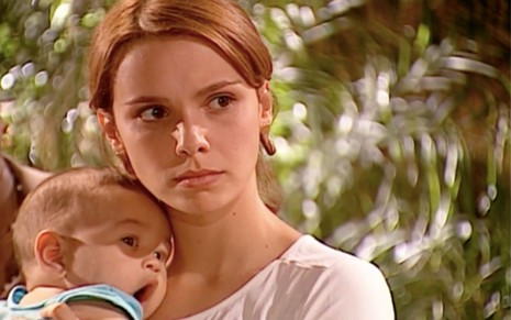 Débora Falabella em cena de O Clone: atriz segura bebê nos braços e olha para alguém fora do quadro
