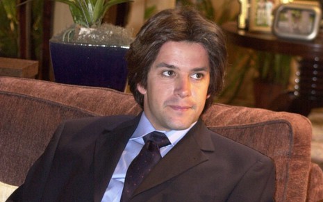 Murilo Benício em cena de O Clone: ator está de terno, sentado e olha com expressão séria para alguém fora do quadro