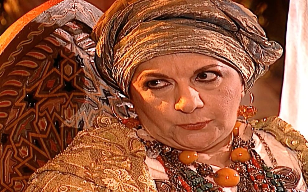 Jandira Martini caracterizada como Zoraide em O Clone; atriz usa turbante dourado, colares de contas e roupas banhadas de ouro. Ela tem os olhos arregalados enquanto encara Stênio Garcia, o Ali --fora de quadro.