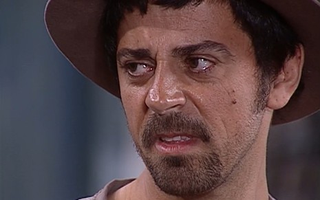 Taumaturgo Ferreira, caracterizado como Januário, tem o semblante desconfiado enquanto encara Joaquim (Carlos Vereza) de rabo de olho em cena de O O Cravo e a Rosa