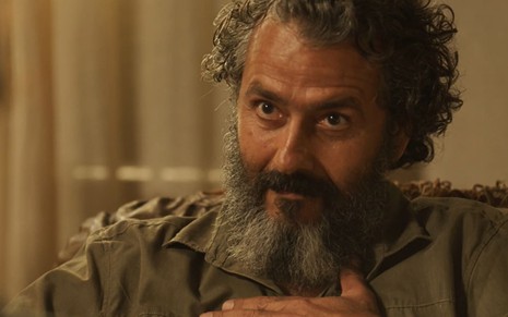 Marcos Palmeira caracterizado como José Leôncio: ator tem os cabelos e a barba longos e grisalhos; ele tem a expressão séria e uma das mãos no peito em cena de Pantanal