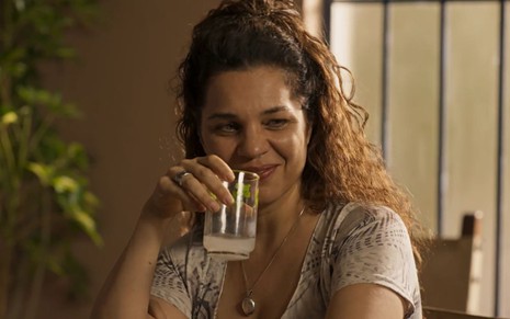 A atriz Isabel Teixeira com copo na mão e sorriso de boca fechada em cena da novela Pantanal