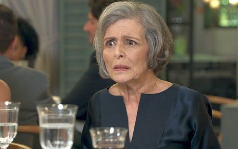 Sabine (Irene Ravache) com expressão de desespero em uma mesa de restaurante em cena de Pega Pega