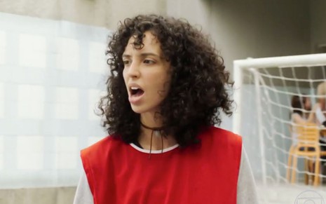 Agnes Brichta em cena de Quanto Mais Vida, Melhor!: atriz está com a boca aberta em sinal de descaso, usa colete vermelho e olha para alguém fora do quadro