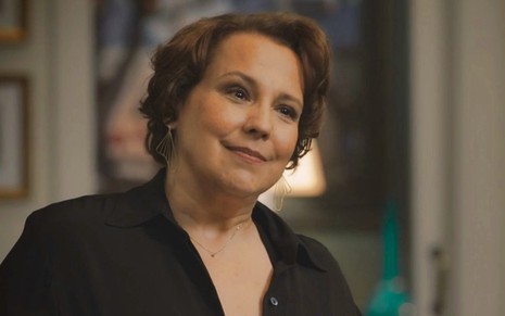 Ana Beatriz Nogueira usa camisa preta e faz uma expressão de deboche em cena da novela Todas as Flores como Guiomar