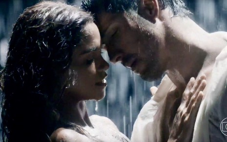 Lucy Alves simula romance, com um quase beijo, em cena com Romulo Estrela; eles estão de branco em um ambiente escuro e com chuva