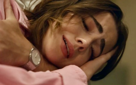 A atriz Jade Picon está simulando choro com a cabeça apoiada em braço e os olhos fechados em cena de Travessia como Chiara
