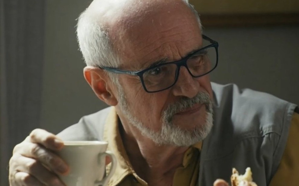 O ator Marcos Caruso segura xícara e olha para o lado em cena da novela Travessia como o professor Dante