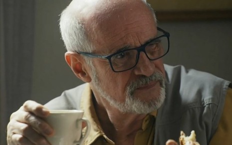 O ator Marcos Caruso segura xícara e olha para o lado em cena da novela Travessia como o professor Dante