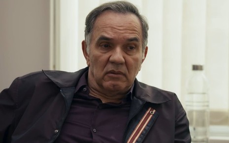 Humberto Martins caracterizado como Guerra em Travessia; ele tem o semblante firme e usa uma camisa preta e um agasalho azul em cena da novela