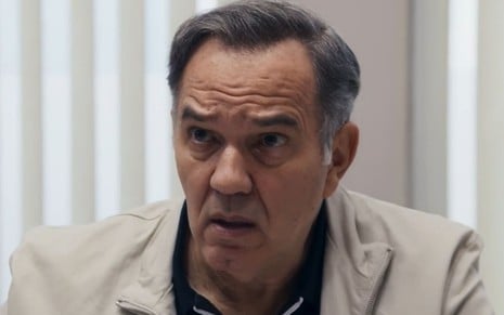 Humberto Martins caracterizado como Guerra em Travessia; ele tem o semblante preocupado e usa uma camiseta preta e uma jaqueta bege em cena da novela
