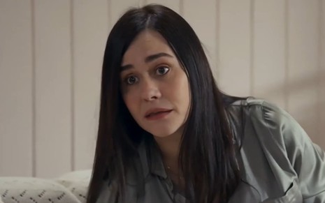Alessandra Negrini tem o semblante perturbado em cena de Travessia; ela usa uma camisa cinza e tem os olhos arregalados e a boca aberta