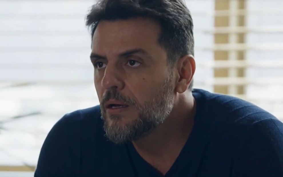 Rodrigo Lombardi caracterizado como Moretti; ator tem as sobrancelhas franzidas e o rosto comprimido em cena de Travessia