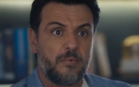 O ator Rodrigo Lombardi usa terno azul claro e faz uma expressão de espanto em cena de Travessia como Moretti