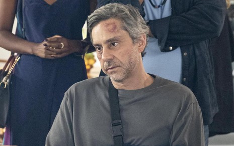 O ator Alexandre Nero usa moletom cinza e exibe hematomas no rosto em cena da novela Travessia como o personagem Stenio