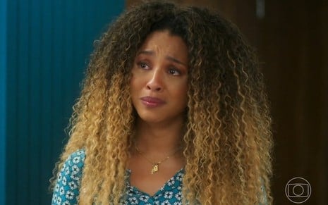 A atriz Sheron Menezzes está chorando em cena de Vai na Fé na qual está com blusa azul com estampa e cabelos soltos