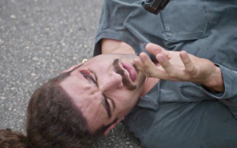 O ator Caio Castro está deitado no chão em gravação de cena de Todas as Flores na qual seu personagem é surrado