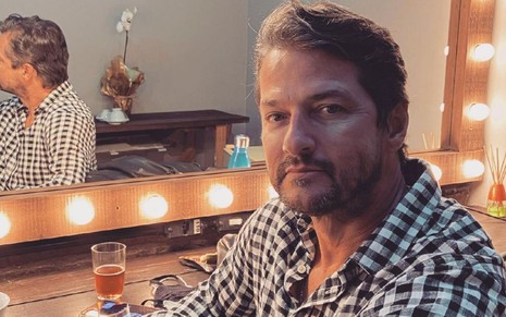 Marcelo Serrado em foto publicada no Instagram: sentado, ator está em penteadeira com camisa quadriculada