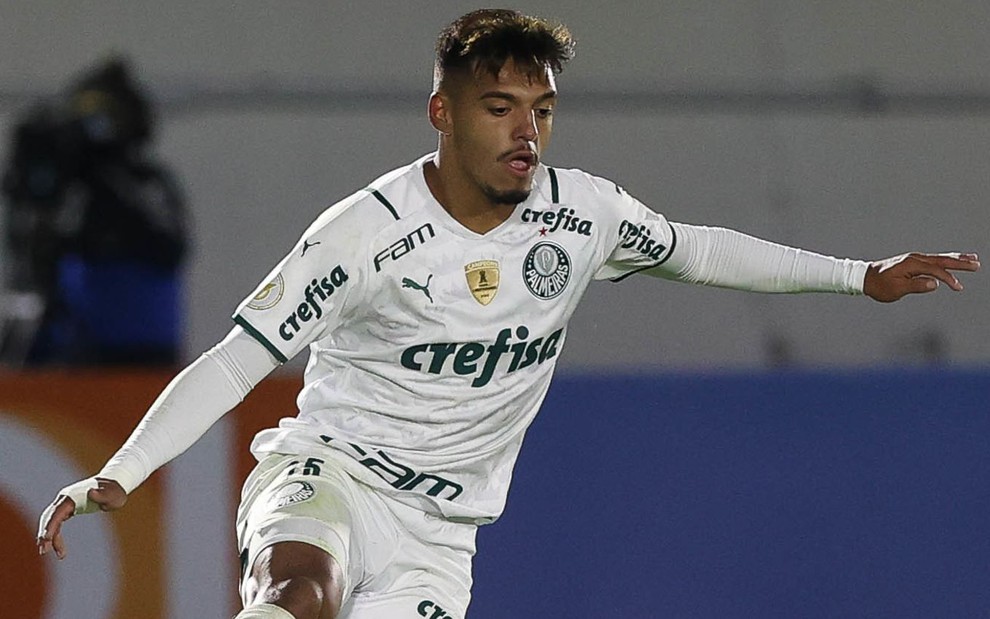 Gabriel Menino com uniforme branco do Palmeiras com os braços um pouco levantados em movimento em campo em partida
