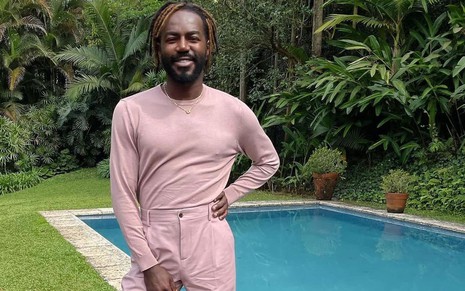 De blusa de manga comprida e calça comprida rosa, Jonathan Azevedo posa em frente a uma piscina