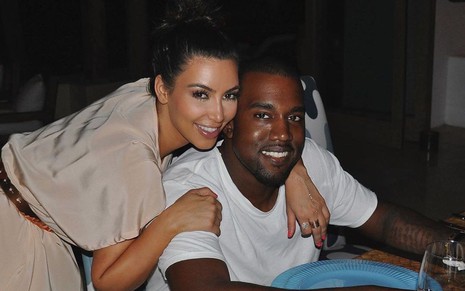 Kim Kardashian de vestido bege abraçada a Kanye West, de camiseta branca
