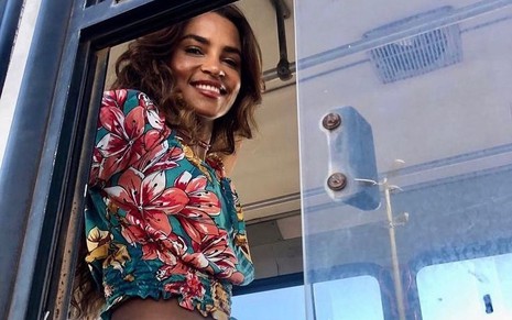 A atriz Lucy Alves, protagonista de Travessia, posa caracterizada dentro de um ônibus