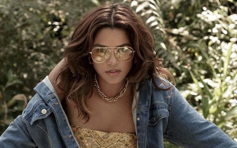 A atriz Lucy Alves, protagonista de Travessia, posa de jaqueta jeans e óculos de sol