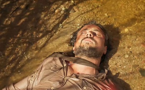 O ator Sergio Guizé como Zé Paulino em Mar do Sertão; ele está deitado, de olhos fechados, com o cabelo molhado, à beira de um rio