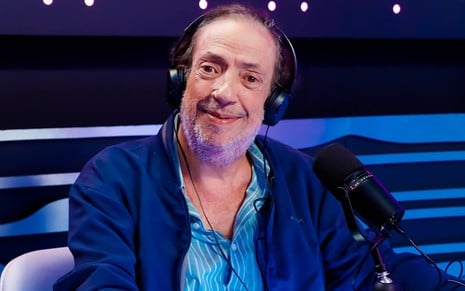 Marcos Oliveira em estúdio de gravação, com terno e camisa azuis, fones de ouvido