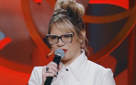 A cantora Marília Mendonça de óculos e segurando um microfone