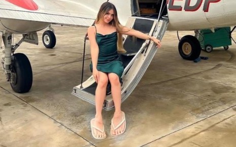Melody sentada na escada de um avião pequeno, pés dela aparecem enormes na foto
