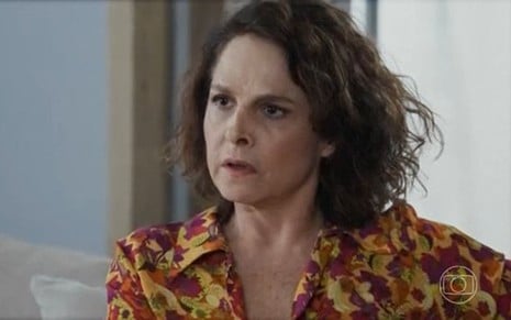 Em cena de Travessia, Drica Moraes está falando com alguém com expressão de surpresa; ela usa blusa estampada