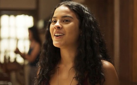 A atriz Bella Campos como Muda em Pantanal; ela está olhando para frente e sorrindo enquanto conversa