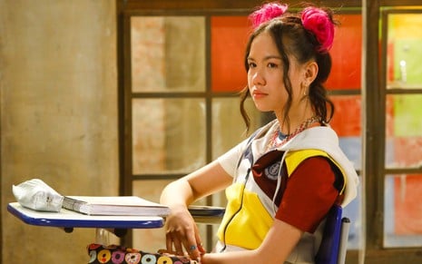 A atriz Bella Chiang sentada em cadeira escolar, de uniforme, em cena da novela Poliana Moça