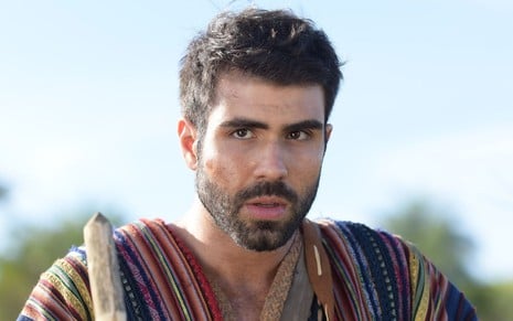 Juliano Laham em cena de Gênesis: ator está caracterizado com túnica com listras coloridas e segura um cajado na mão direita