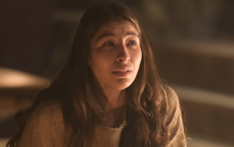 Sentada em uma cadeira em tenda, Tamar (Juliana Xavier) chora em cena de Gênesis