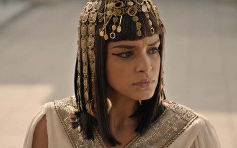 A atriz Kizi Vaz com expressão de raiva como a Kamesha com um peruca adornada com adereços em ouro como a Kamesha em cena de Gênesis