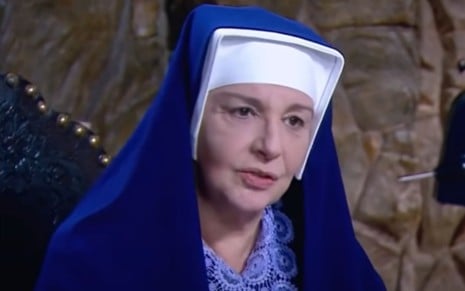 Eliana Guttman grava cena vestida de freira, com expressão tensa, como Madre Superiora