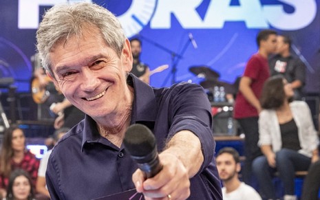 Serginho Groisman sorri e aponta o microfone para a câmera no estúdio do Altas Horas