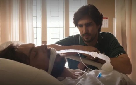 Zé Paulino (Sergio Guizé) está no leito do hospital e é observado por Tertulinho (Renato Góes) em cena da novela Mar do Sertão