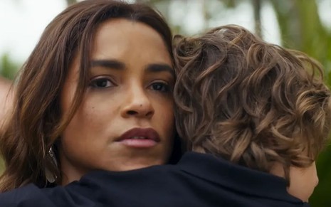 Os atores Lucy Alvesz e Vicente Alvite como Brisa e Tonho em Travessia; eles estão abraçados, enquanto ela olha para frente atentamente e ele a abraça de costas