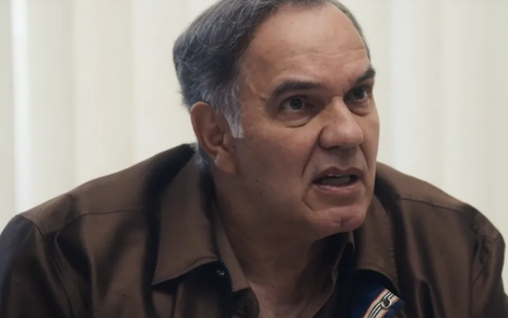 Em cena de Travessia, Humberto Martins está falando com alguém a sua frente com ar de preocupação; ele usa blusa de manga comprida marrom