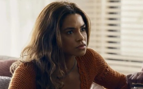 Em cena de Travessia, Lucy Alves usa blusa marrom; ela parece estar falando com alguém, preocupada