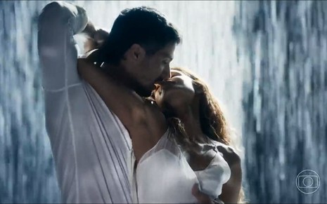 Os atores Romulo Estrela e Lucy Alves como Oto e Brisa em Travessia; eles estão debaixo da chuva, quase se beijando, enquanto ela o seguro no pescoço