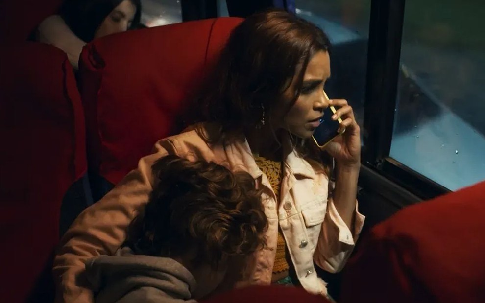 Os atores Vicente Alvite e Lucy Alves como Tonho e Brisa em Travessia; ele está deitado no colo dela, sentados em poltronas de um ônibus, enquanto ela fala no celular