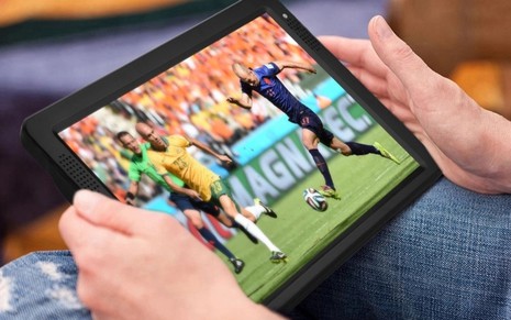 Consumidor vendo um jogo de futebol na TV Portátil apoiada no colo